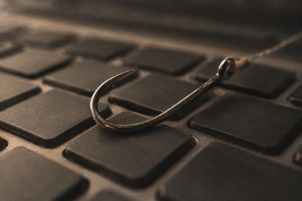 A fishing hook resting on a laptop keyboard, a visual metaphor for phishing